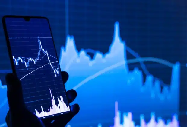 a person holding a cell phone in front of a stock chart